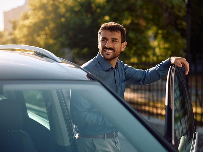 Un uomo sorride appoggiato alla portiera dell'automobile
