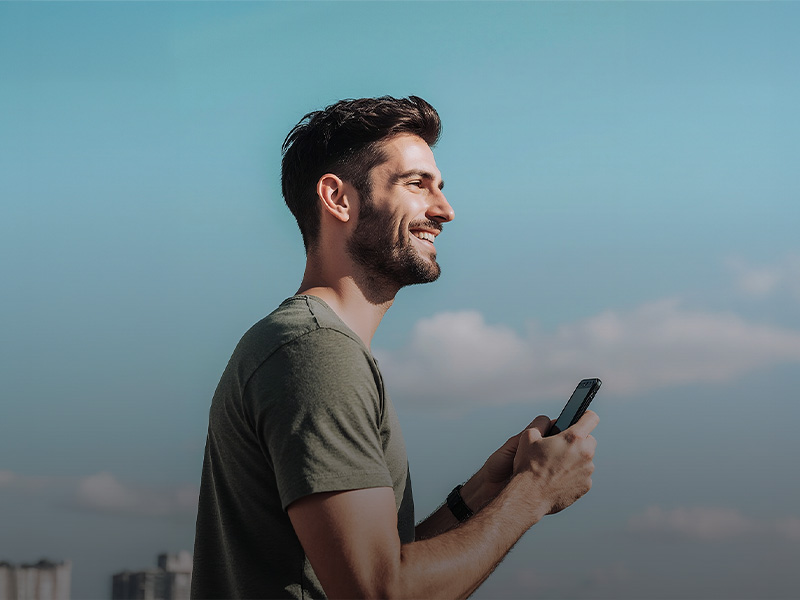 Giovane uomo sorridente con lo smartphone in mano: maggiore controllo sui bonifici con la verifica del beneficiario