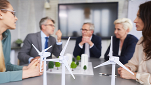 Un gruppo di uomini e donne intorno a un tavolo studiano un progetto con miniature di edifici e pale eoliche